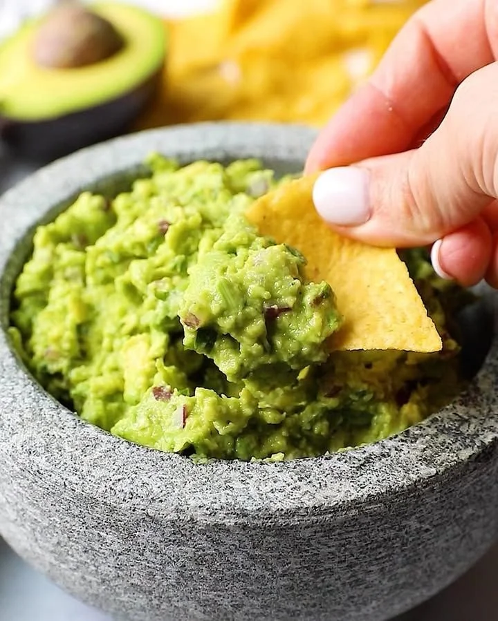 Bowl of freshly made guacamole with avocados, tomatoes, and cilantro